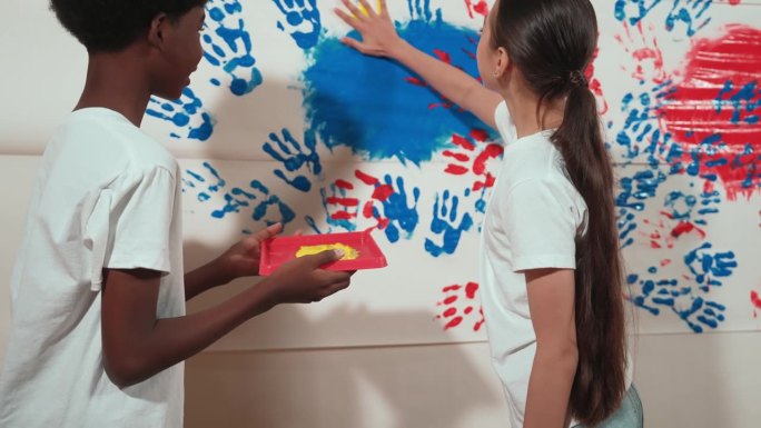 快乐的孩子们把手放在彩色托盘里，贴在墙上。启迪
