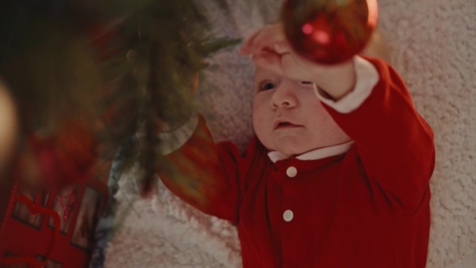 宝宝躺在家里的地毯上玩挂在圣诞树上的小玩意的高角度手持镜头