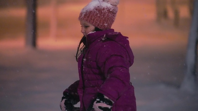 穿着紫色夹克的快乐少女在公园里漫步，夜雪飘飘