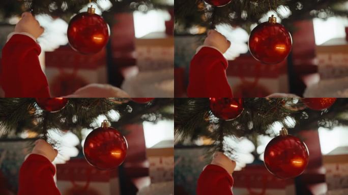 剪短的小男孩的手在家里玩挂在圣诞树上的闪亮的红色小玩意