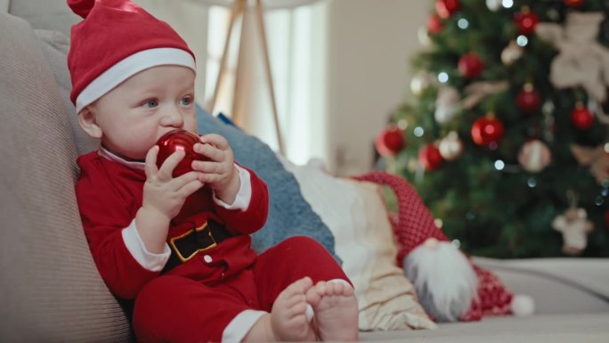 裁剪的妈妈的手在家里的沙发上给穿着圣诞老人服装的小男孩红色小玩意