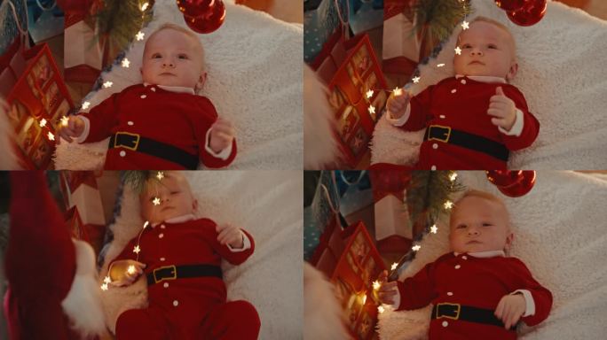 高角度手持拍摄的男婴穿着圣诞老人服装，躺在家里的地毯上玩圣诞灯