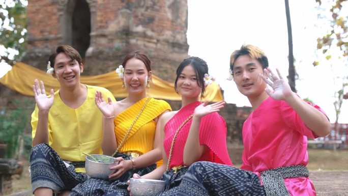 在泰国泼水节期间，一群穿着传统泰国服装的年轻人在镜头前交谈、挥手