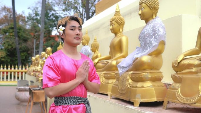 一个穿着泰式粉色衬衫的年轻人。在泰国宋干节期间，向佛像沐浴仪式致敬。