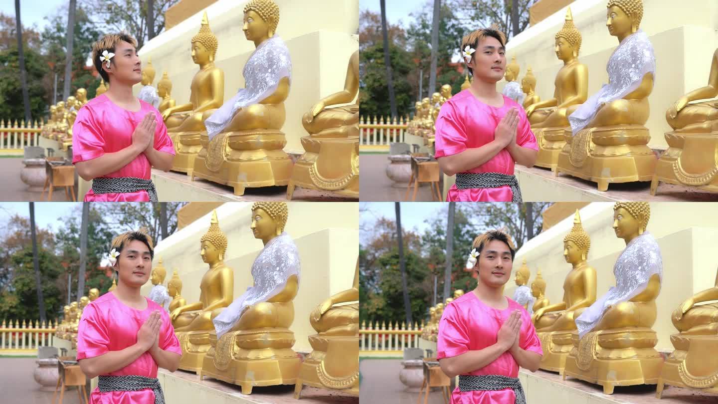 一个穿着泰式粉色衬衫的年轻人。在泰国宋干节期间，向佛像沐浴仪式致敬。