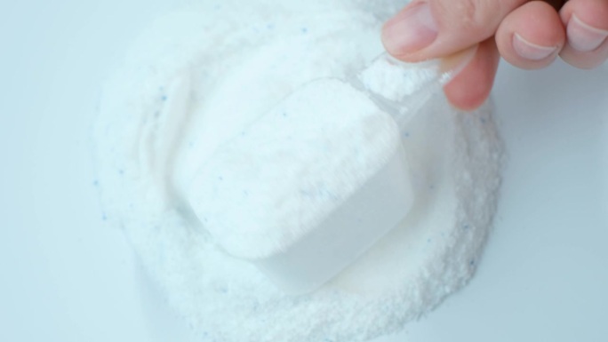 女性手拿着一勺洗衣粉，白色背景特写。