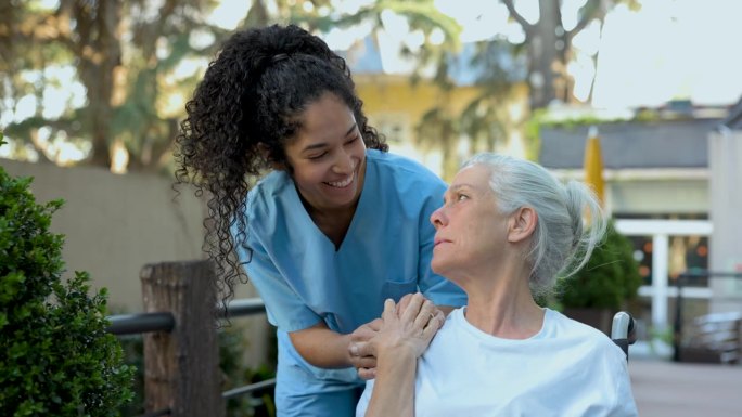 在辅助生活设施中，关怀的护士与女老年病人手牵着手，两人愉快地交谈