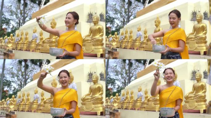 穿着泰国传统服装的漂亮女孩对着镜头微笑。泰国泼水节期间为佛像沐浴的仪式