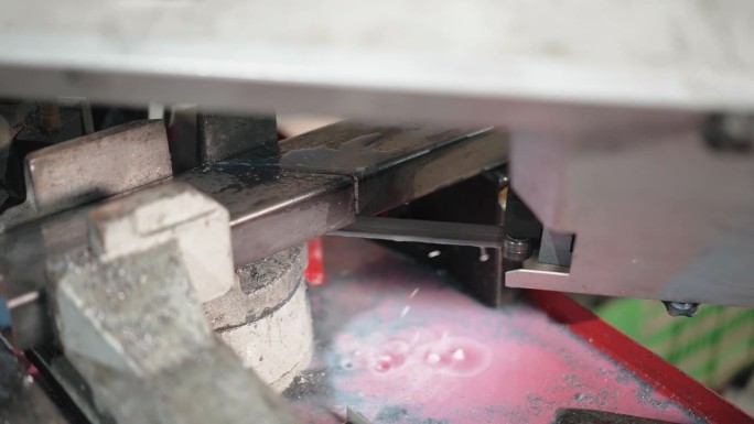 锋利的刀片切割金属板材上的两个部分在水冷却系统下，冷却液水滴和一些金属残余物在切割机下。自动化五金工