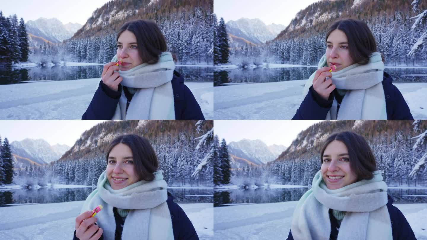 Zgornje Jezersko的雪林和山脉中，在Flozen湖附近，微笑的年轻女子涂唇膏的照片