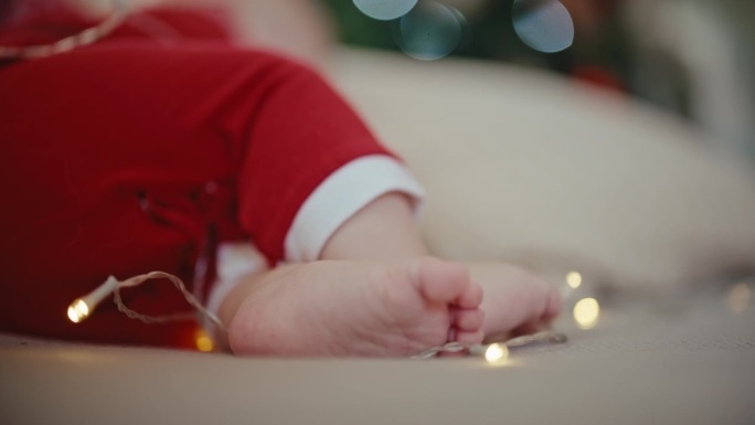 手持拍摄的男婴穿着圣诞老人服装躺在沙发上，家里有圣诞灯