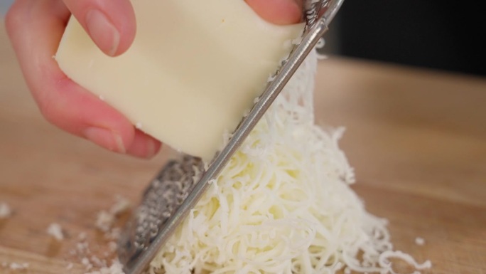 马苏里拉奶酪是用细磨碎器在木桌上磨碎的。特写镜头