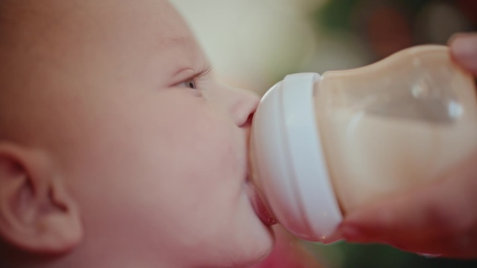 圣诞期间，小男孩在家里用妈妈喂的奶瓶喝牛奶的特写
