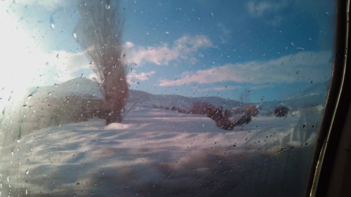 一个男人一边看着冬天的景色，一边用手擦着雾气蒙蒙的车窗。