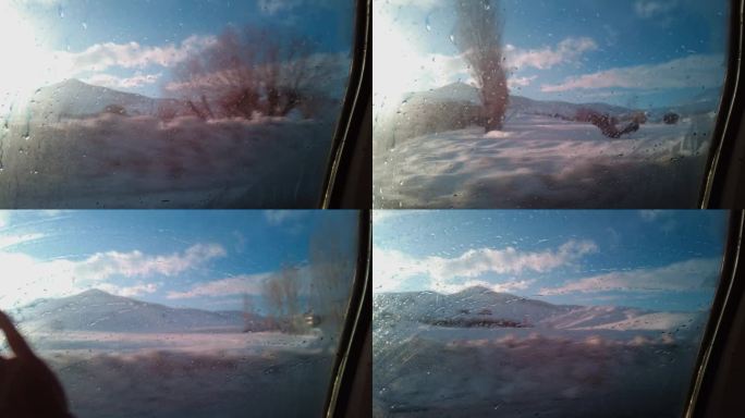 一个男人一边看着冬天的景色，一边用手擦着雾气蒙蒙的车窗。