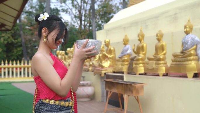 一位穿着传统泰国服装的漂亮女孩正在祈祷。泰国泼水节期间为佛像沐浴的仪式