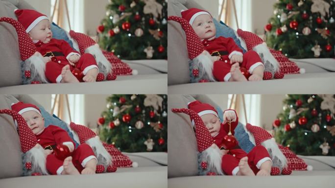 手持拍摄的圣诞老人服装的男婴在沙发上玩红色小玩意在家里的圣诞节