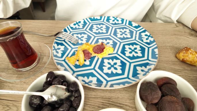 特写:在土耳其早餐桌上，一个女人用勺子把大蒜香肠炒蛋端到她的蓝色盘子里。一家人愉快地吃了一顿早餐。土