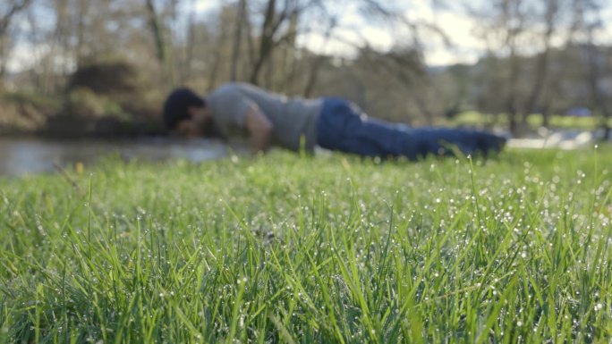 在一个晴朗的日子里，一个瘦骨嶙峋的年轻人在草地上做俯卧撑。