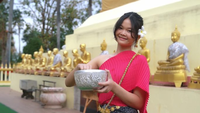 穿着泰国传统服装的漂亮女孩对着镜头微笑。泰国泼水节期间为佛像沐浴的仪式