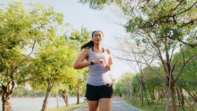 一个意志坚定的女人带着健身追踪器在阳光明媚、绿树成荫的公园里跑步