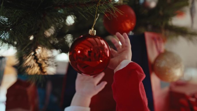 手持拍摄的小男孩的手与挂在家里圣诞树上的红色闪亮小玩意玩耍