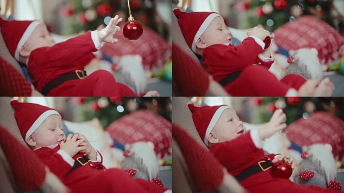 穿着圣诞老人服装的快乐小男孩在家里玩妈妈送的红色小玩意的手持照片