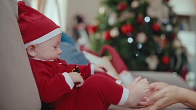 顽皮快乐的小男孩穿着圣诞老人的服装，坐在家里的沙发上和妈妈玩耍