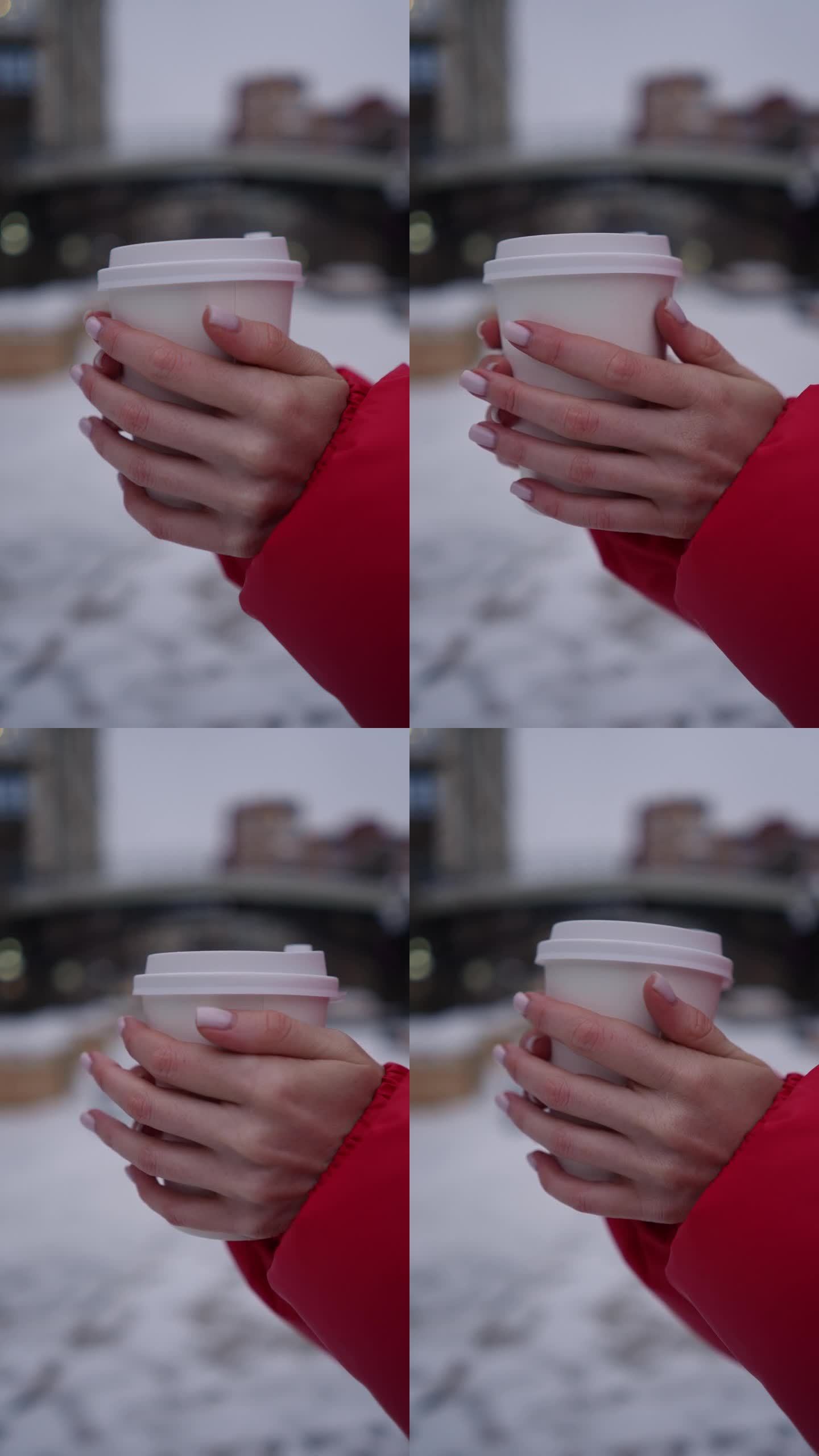 这是一张垂直特写照片，照片上是一个无法辨认的身穿红色夹克的女人，手里拿着一杯外卖咖啡或茶，摄于下雪的