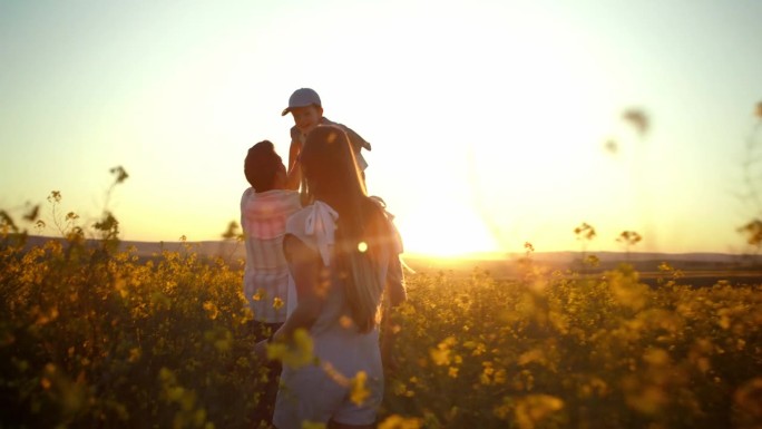 夕阳下，妈妈、爸爸和孩子在乡村的花丛中拥抱、自由或亲密。家庭冒险农场与快乐的男人，女人和男孩走在大自