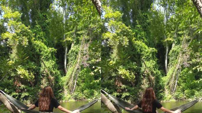 在茂密的森林里，翠绿的溪边，一个女人在吊床上摇摆。这是夏天和阳光明媚的一天。小溪里有一张野餐桌。她转