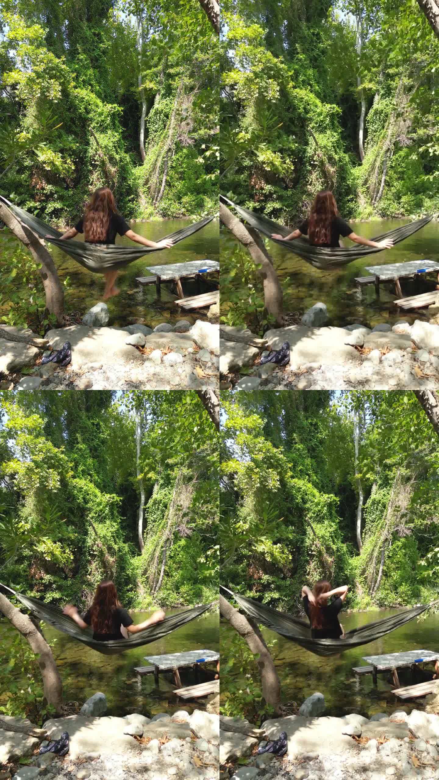 在茂密的森林里，翠绿的溪边，一个女人在吊床上摇摆。这是夏天和阳光明媚的一天。小溪里有一张野餐桌。她转