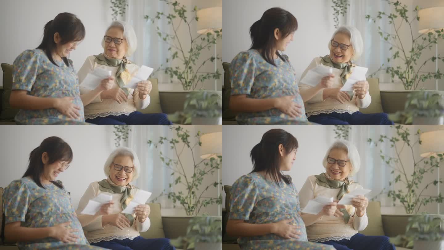 愉快的孕妇和她的母亲坐在窗边聊天怀孕和笑在家里