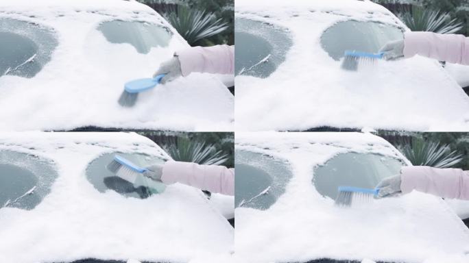 一位妇女正在用刷子清理她的汽车上的积雪。清洁风挡玻璃