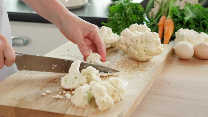 女厨师在厨房用锋利的刀将菜花切成小块，木桌上摆放着蔬菜、健康食品、家常菜、减肥食品、减肥食品、素食食