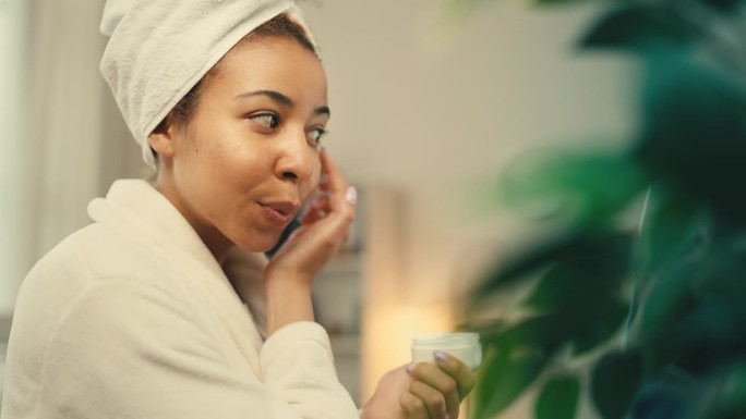 微笑的非裔美国女性在使用眼霜、美容和护肤品