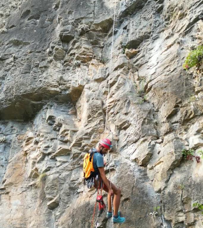 攀爬者用凿岩机和旋锤在攀爬绳上开辟一条新的攀爬路线后，用绳子往下走。登山者戴着红色的头盔。