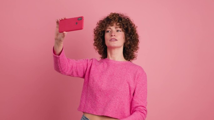 开朗的女子用粉红色背景的手机自拍