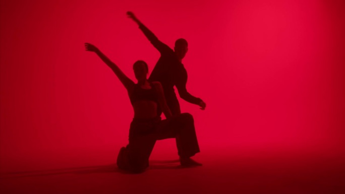 专业舞蹈编导在工作室的红色霓虹灯背景上跳舞。男女舞者表现出缓慢的动作，双人舞，二人转。青少年现代舞学