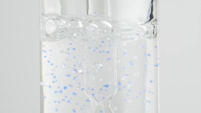 滴剂与化妆品精华液混合使用。血清中有蓝色颗粒。瓶子里的气泡。宏。缓慢的运动。