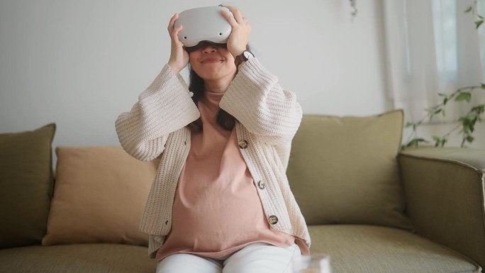 在舒适的客厅里，一位孕妇坐在沙发上，头上戴着VR眼镜。