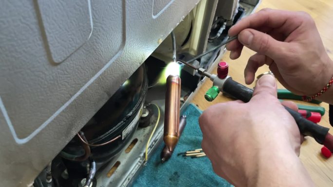 通过给氟利昂管充电来修复冰箱冷却不足的问题。师傅用烙铁把一根管子接上氟利昂。