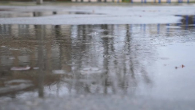 小雨滴落在柏油路上的大水坑里。雨滴溅落在反光的水面上。春季或秋季雨季。宁静场景的概念。慢动作