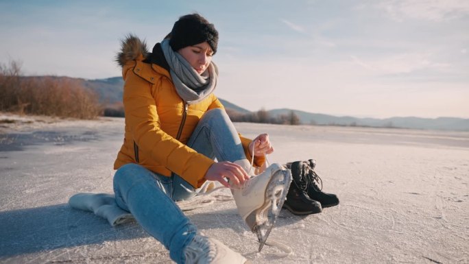 穿着保暖衣服的年轻女子坐在结冰的湖面上系鞋带