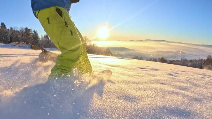 镜头:在金色的冬日日出中，滑雪板运动员和他的狗一起骑着粉雪