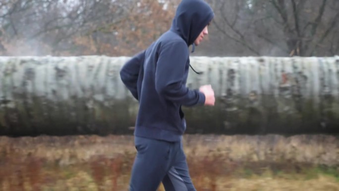 穿着运动服的健壮运动员在阴天沿着小路慢跑。年轻的运动员在雨中沿着柏油路奔跑。运动健将在户外做有氧运动
