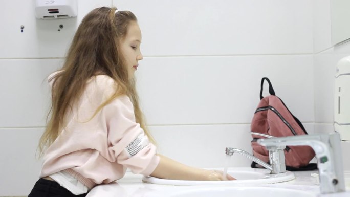 一个十几岁的小女孩在浅色的背景下洗手。孩子们的卫生。女学生在购物中心或咖啡馆的厕所里。