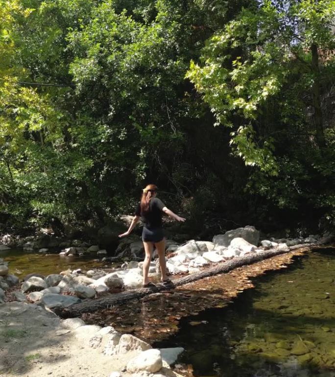 夏天，一名妇女正踩着一根木头在溪水上过河。水是清澈的。她转过身去。她在努力保持平衡。