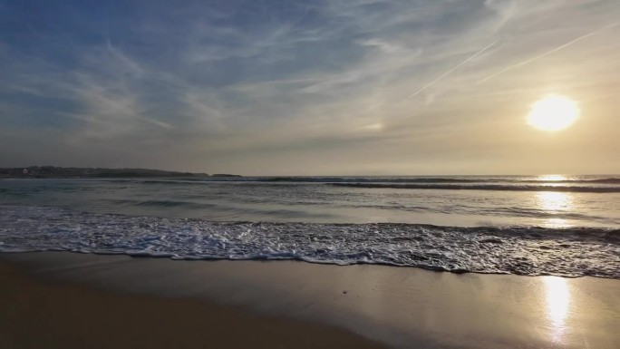 海浪翻滚到沙滩上，背景是蓝色的天空和戏剧性的雷云，日落，美丽的风景