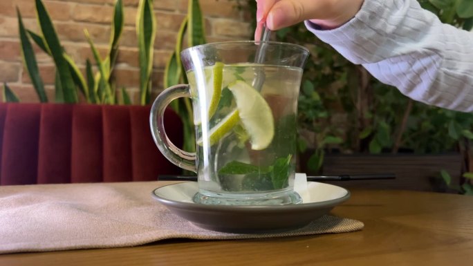 一个女人在白色的桌子上用玻璃茶壶泡水果热茶，里面有薄荷和柠檬。健康的热饮。